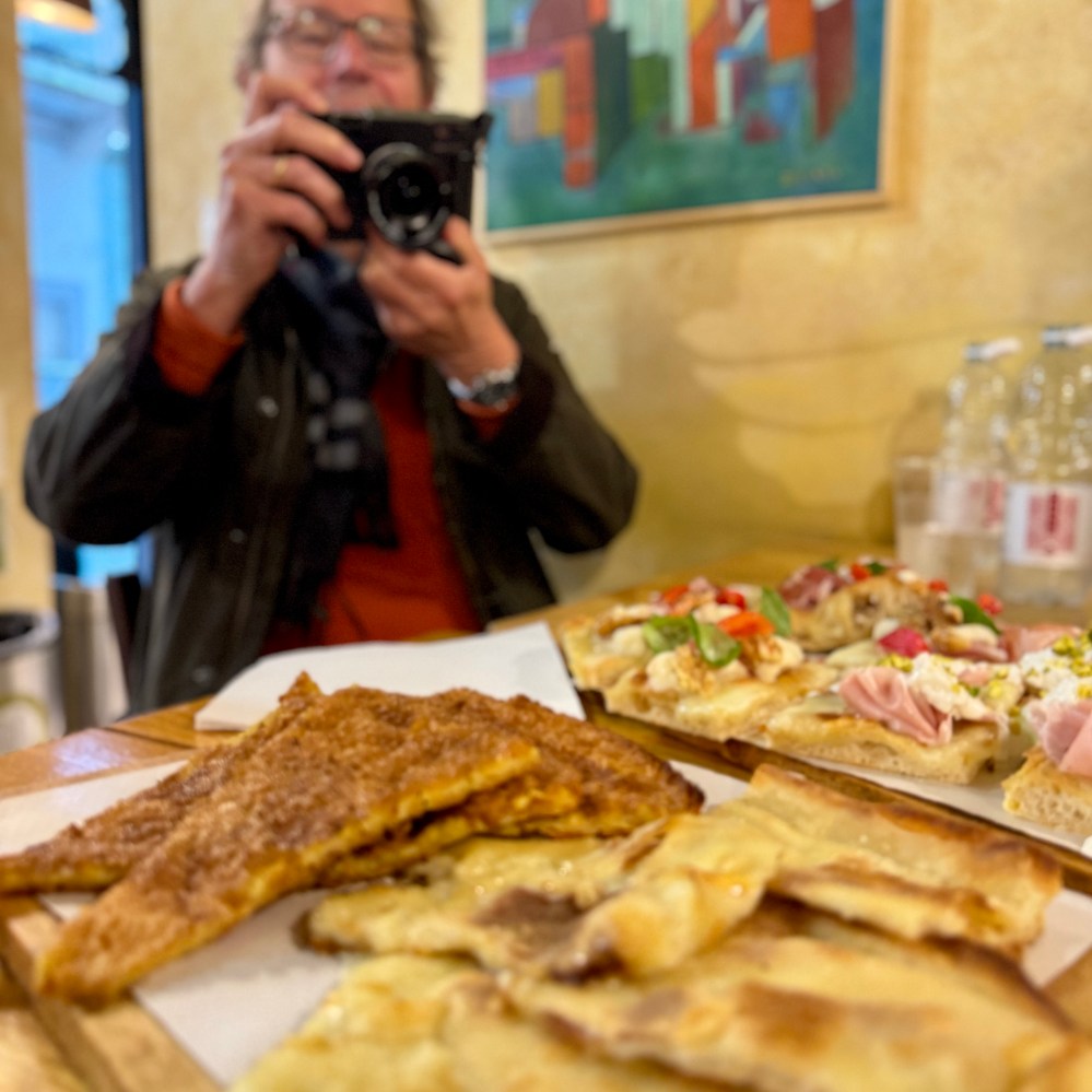 A person taking a photo of various pizzas on a wooden table.